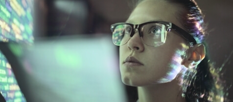 Young woman with spectacles intently studying a computer screen